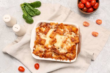 Gri grunge arka planda lezzetli makarna, domates ve ıspanak yapraklı fırın yemeği.