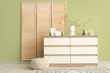 İçinde ağaç dalları olan vazolar ve şenlikli oturma odasındaki çekmecelerin üstünde Paskalya yumurtaları.