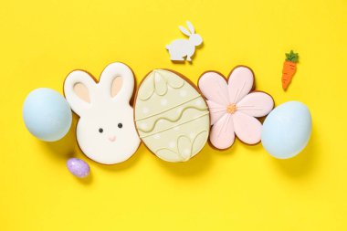 Yumurtalı kompozisyon, çiçek şeklinde Paskalya kurabiyeleri, sarı arka planda yumurta ve tavşan.