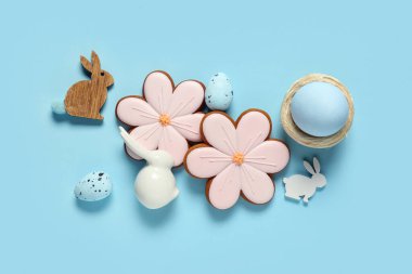 Yumurtalı kompozisyon, dekoratif tavşanlar ve mavi arka planda çiçek şeklinde Paskalya kurabiyeleri.