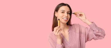 Güzel genç bir kadın pembe arkaplan üzerine rimel sürüyor ve mesaj için yer açıyor.