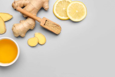 Taze zencefil kökü, limon dilimleri ve arkaplanda kurumuş toz olan ahşap kepçe.