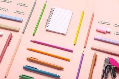 Pembe arka planda farklı kırtasiye malzemesi içeren defter.