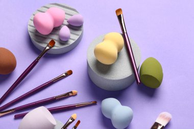 Dekoratif podyumlar makyaj fırçaları ve eflatun arka planda süngerler