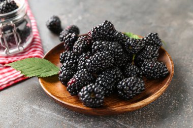 Gri arka planda taze böğürtlenli ahşap tabak.