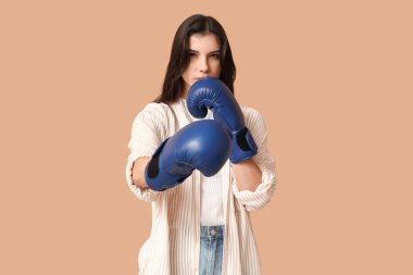 Young woman in boxing gloves on beige background. Feminism concept