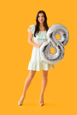 Sarı arka planda 8 şeklinde gümüş renkli hava balonu olan güzel genç bir kadın. Uluslararası Kadınlar Günü