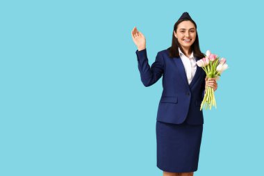 Mavi arka planda bir buket çiçekle el sallayan genç hostes portresi. Uluslararası Kadınlar Günü