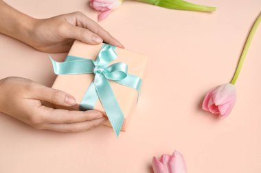 Hediye kutusu olan kadın eller ve pembe arka planda güzel laleler. Uluslararası Kadınlar Günü