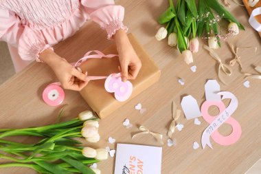 Arkaplanda Uluslararası Kadınlar Günü için hediye kutusu, paketleme malzemeleri ve lale çiçekleri olan bir kadın.