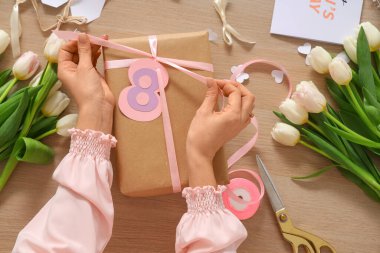 Uluslararası Kadınlar Günü için hediye paketi ve lale çiçeği hazırlayan kadın ahşap arka planda, yakın plan.