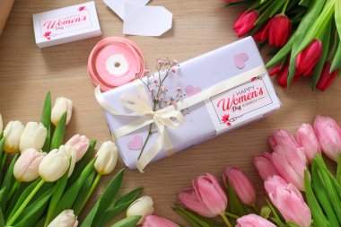 Ahşap zemin üzerinde Uluslararası Kadınlar Günü için hediye paketi, paketleme malzemeleri ve güzel lale çiçekleri olan kompozisyon