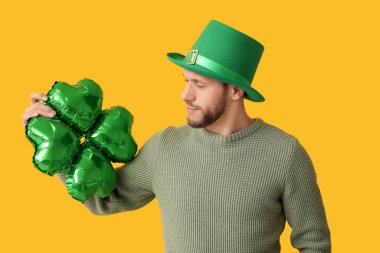 Sarı arka planda yonca şeklinde hava balonu olan cüce şapkalı genç adam. Aziz Patrick Günü kutlaması