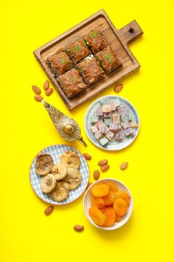 Sarı zemin üzerinde geleneksel Doğu tatlıları ve Ramazan ayı için Alaaddin lambası kompozisyonu