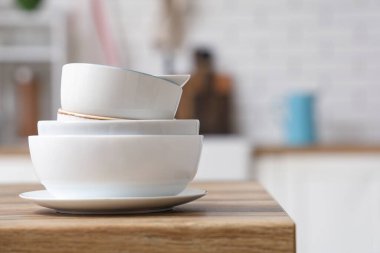 Mutfaktaki ahşap masada beyaz, temiz sofra takımı yığını.