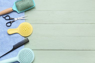 Yeşil ahşap arka planda saç fırçası, tarak ve makaslı havlu.