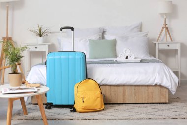 Yatağın yanında bavul ve sırt çantalı bir otel odası.