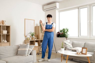 Erkek işçi odada klimayı tamir ediyor.