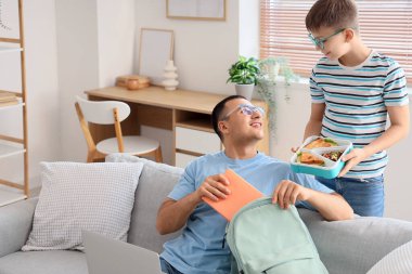 Babası ve okul çantalı küçük oğlu sırt çantalarını evde topluyor.