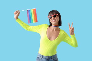Mavi arka planda zafer jesti gösteren LGBT bayrağıyla gökkuşağı dekolteli güzel genç bir kadın.