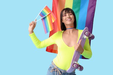Mavi arka planda LGBT bayrakları ve kaykayı olan güzel genç bir kadın.