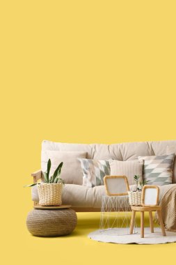 Rahat beyaz kanepe, ev bitkileri ve sarı arka planda halı.