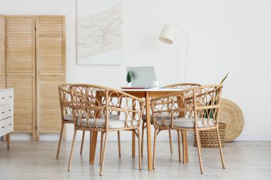 Masa ve hasır sandalyeler yemek odasındaki beyaz duvarın yanında.