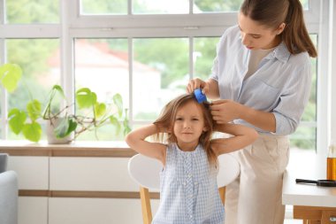 Mother combing her little daughter's hair with pediculosis at home clipart