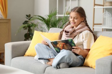 Kitap okuyan ve oturma odasındaki kanepede oturan tatlı kız öğrenci.