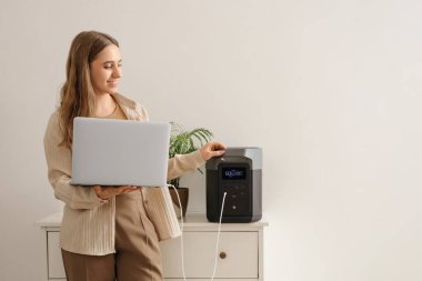 Taşınabilir elektrik santrali ve dizüstü bilgisayarı olan genç bir kadın.