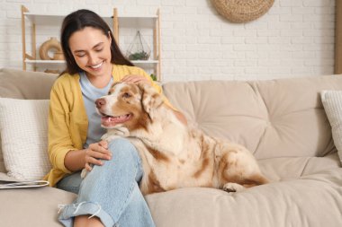 Avustralya çoban köpeği olan genç bir kadın evdeki kanepede oturuyor.