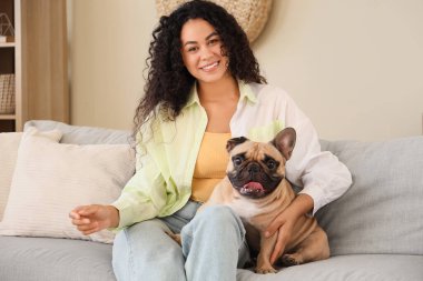 Evdeki kanepede oturan sevimli Fransız bulldoguyla güzel bir Afro-Amerikalı kadın.