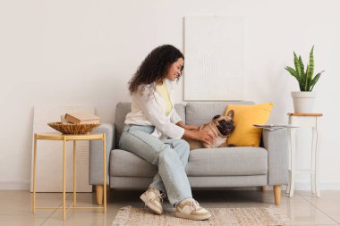 Güzel, genç, Afro-Amerikan bir kadın ve tatlı bir Fransız bulldog 'u oturma odasında kanepede oturuyor.