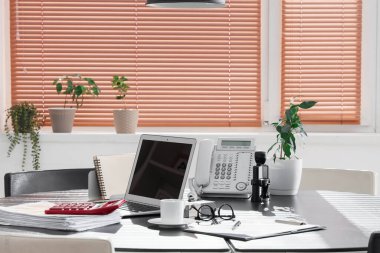 Ofiste kahve fincanı, telefon ve bitki içeren dizüstü bilgisayar.