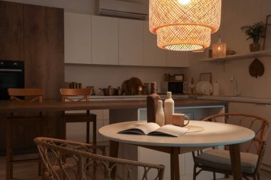 Akşam vakti yemek masası, tezgah ve parlayan lambalar olan karanlık mutfağın içi.