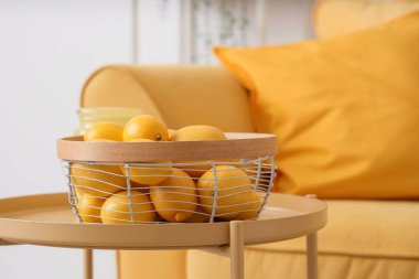 Süslü oturma odasındaki sarı kanepenin yanındaki sepetin üzerinde taze limon var.