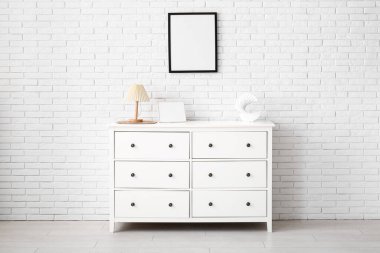 Çekmeceler ve beyaz tuğla duvarda asılı boş bir poster.