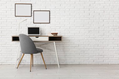Laptoplu masa ve beyaz tuğla duvarda boş posterler