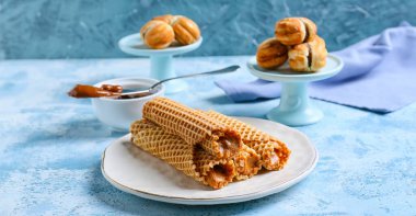 Lezzetli gofret ruloları ve mavi arka planda kaynamış konsantre süt.