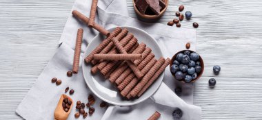 Lezzetli çikolatalı gofret ruloları ve hafif ahşap arka planda yaban mersinli tabak.