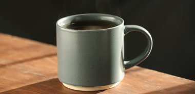 Koyu arka planda, ahşap masada bir kupa sıcak çay.