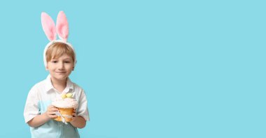 Tavşan kulaklı şirin bir çocuk ve açık mavi arka planda paskalya pastası.