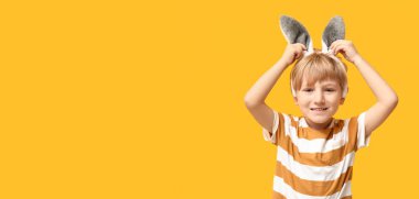 Sarı arka planda paskalya tavşanı kulağı takan şirin bir çocuk.