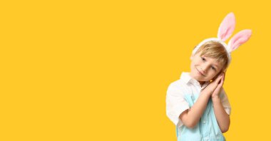 Sarı arka planda paskalya tavşanı kulağı takan şirin bir çocuk.