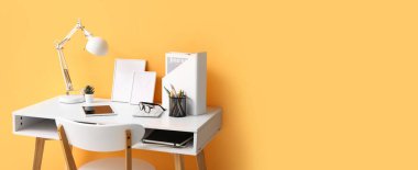 Turuncu duvarın yanında tablet bilgisayarı, lambası ve malzemeleri olan rahat bir iş yeri. Tasarım için pankart