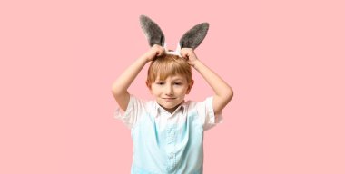 Pembe arka planda Paskalya tavşanı kulağı takan şirin bir çocuk.