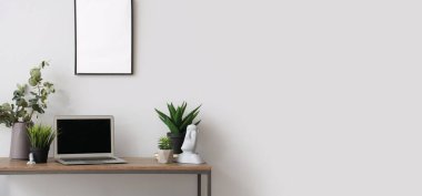 Modern dizüstü bilgisayar ve beyaz duvarın yanındaki masada farklı ev bitkileri. Tasarım için pankart