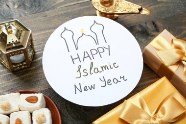 Yazılı kart Mutlu İslami Yıl, tatlılar ve hediye kutuları ahşap arka planda, yakın planda
