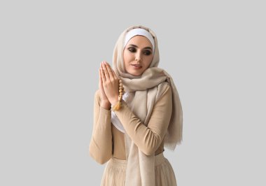 Young Muslim woman praying on light background. Islamic New Year celebration