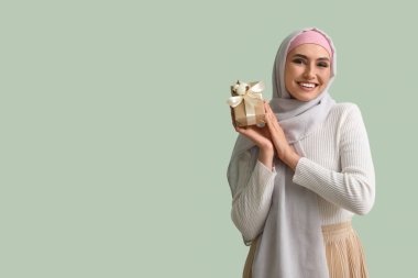 Young Muslim woman with gift on green background. Islamic New Year celebration